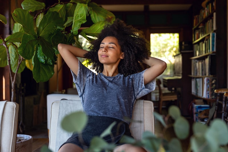 womanwoman happy with new heat pump installation relaxing in chair surrounded by plants woman happy with new heat pump installation