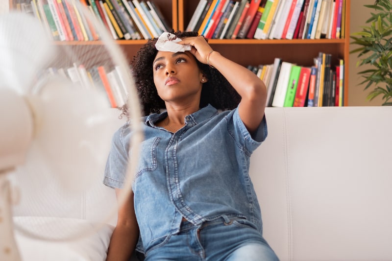 Unhappy Woman Dabbing Her Sweat In Front Of Fan Unhappy Woman Dabbing Her Sweat In Front Of Fan