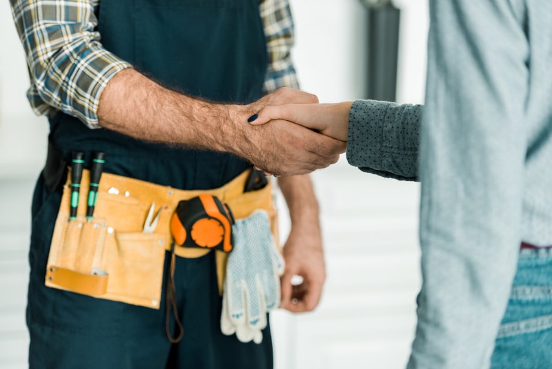 Handshake between contractor wearing tool belt and client Handshake between contractor wearing tool belt and client